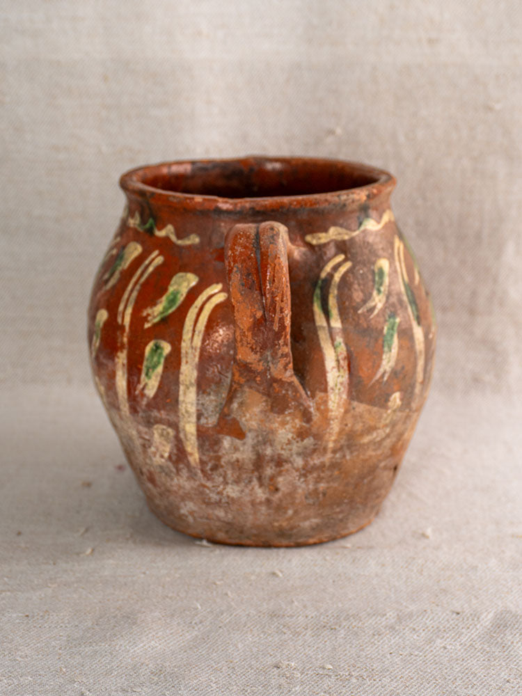 Early 19th century French terracotta slipware pot with single handle and hand painted green and yellow bird motif on fabric.