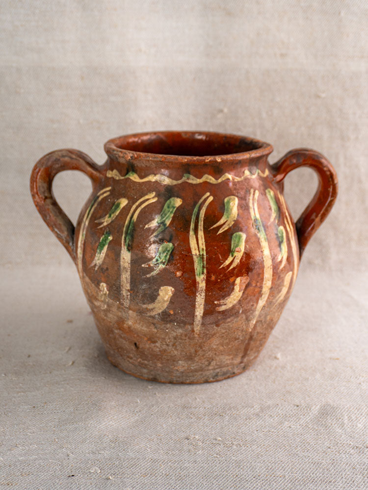 Early 19th century French terracotta pot with jaspé décor and slipware, two handles, on neutral fabric.