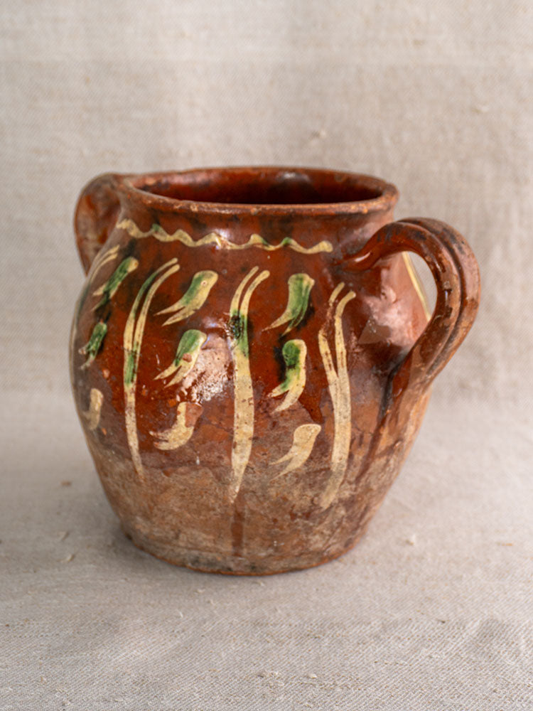 French early 19th-century terracotta pot with Jaspé décor, two handles, yellow, green, and white on beige fabric surface.