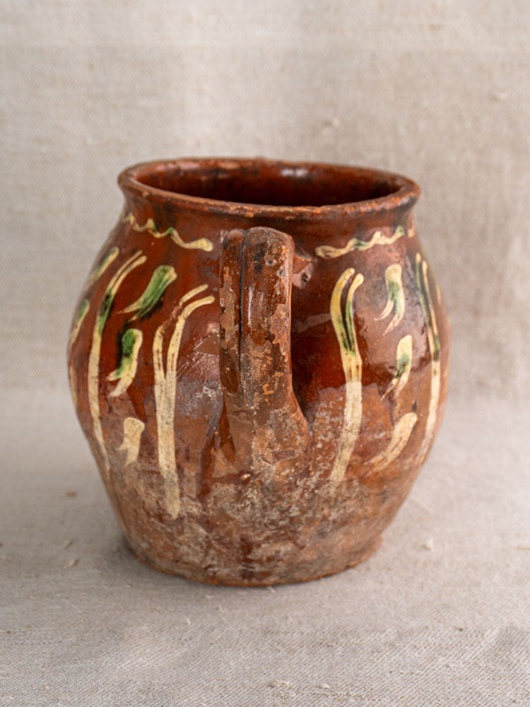 Early 19th century French terracotta pot with yellow and green jaspé slipware, single handle, on beige textured fabric.