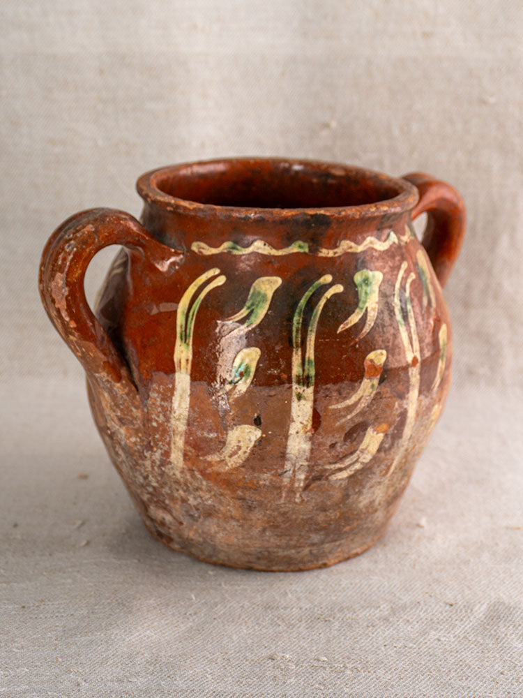 Early 19th century French terracotta pot with brown glaze and cream jaspé slipware, lightly aged, on beige textured fabric.