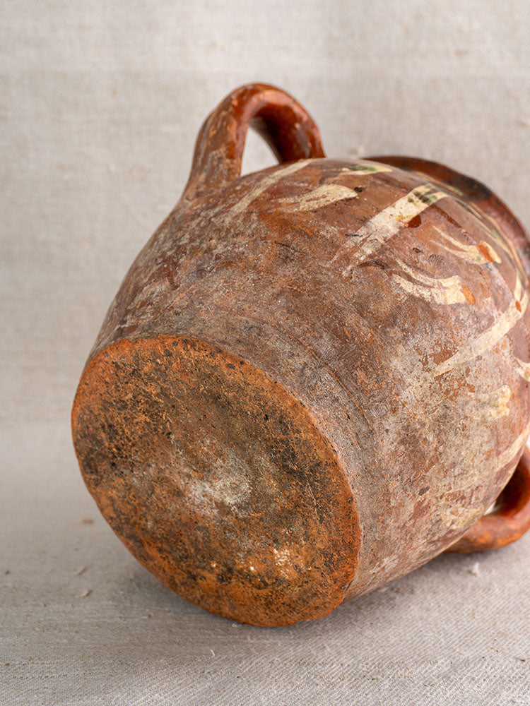 Early 19th century French terracotta slipware pot with jaspé décor, faded brown and cream markings, neutral fabric backdrop.