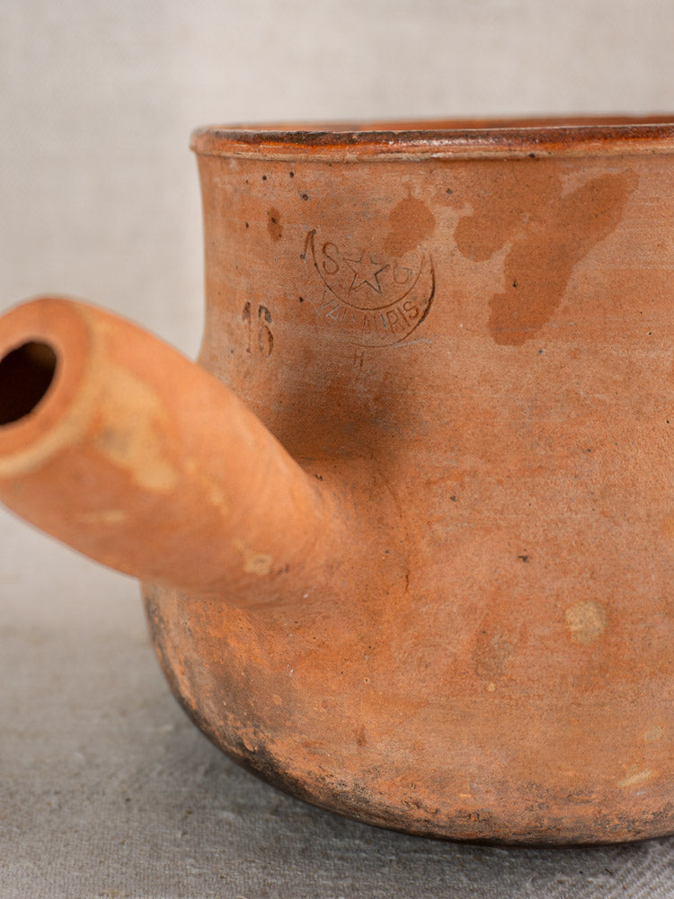 Antique French Vallauris Poêlon terracotta pot with hollow handle, embossed mark, number 16, worn patina, neutral textured backdrop.