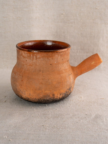 Rustic round terracotta mug with hollow handle, handmade style and darkened base, reminiscent of French Vallauris pottery.