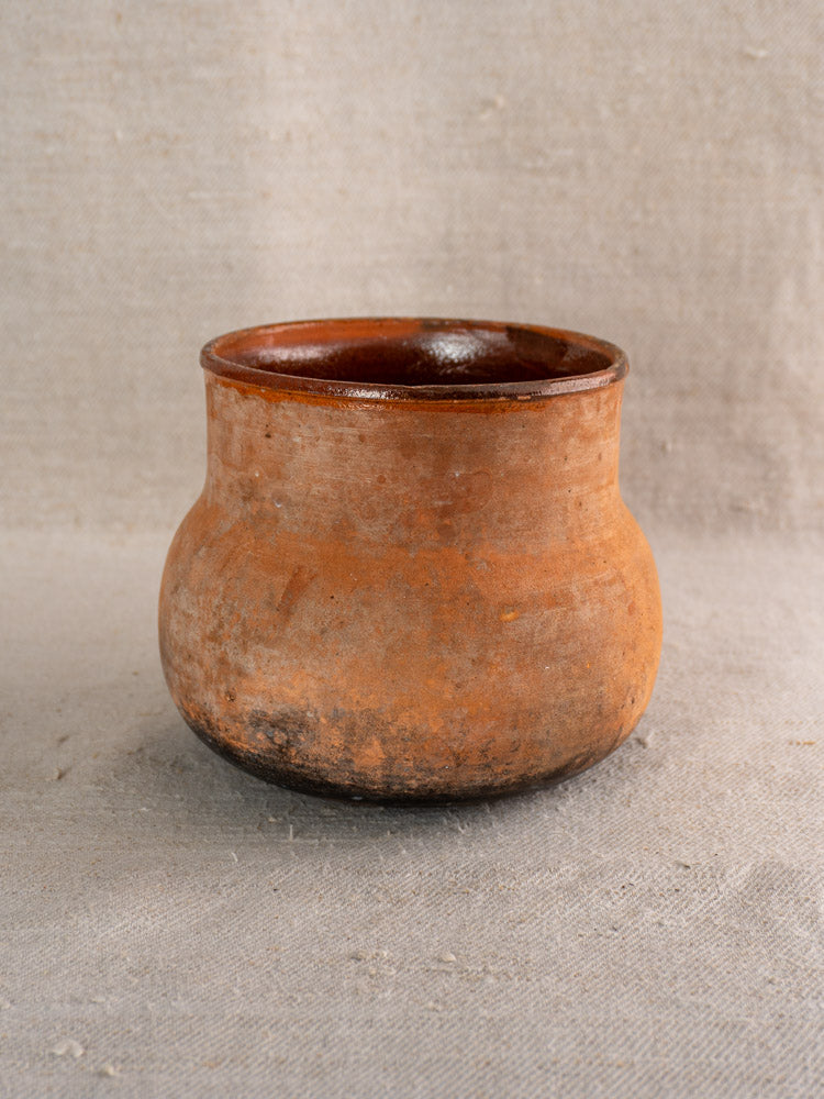 Antique French Vallauris poêlon terracotta pot with hollow handle, wide mouth, and visible rustic patina on beige fabric.