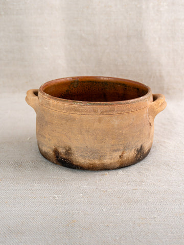 Antique French terracotta hearth cooking pot with side handles and fire-darkened base on textured surface.
