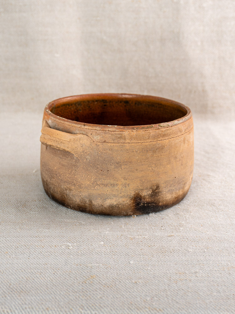Antique French terracotta cooking pot with fire-darkened, glazed finish on a neutral fabric surface.