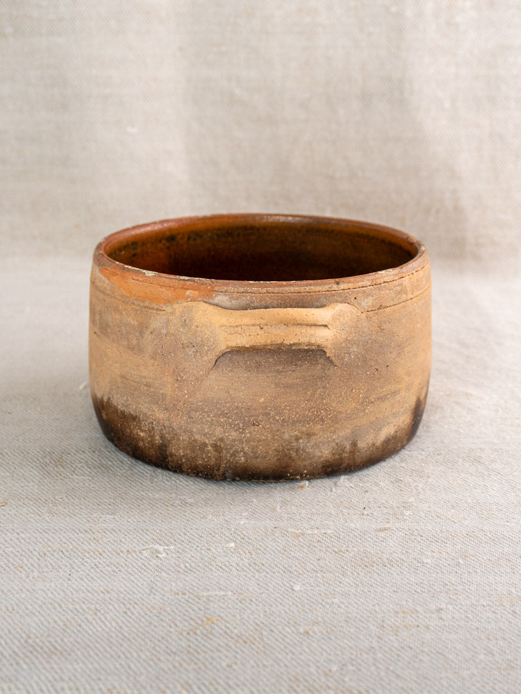 Antique French terracotta hearth cooking pot with glazed finish and rustic carved lines on fabric.