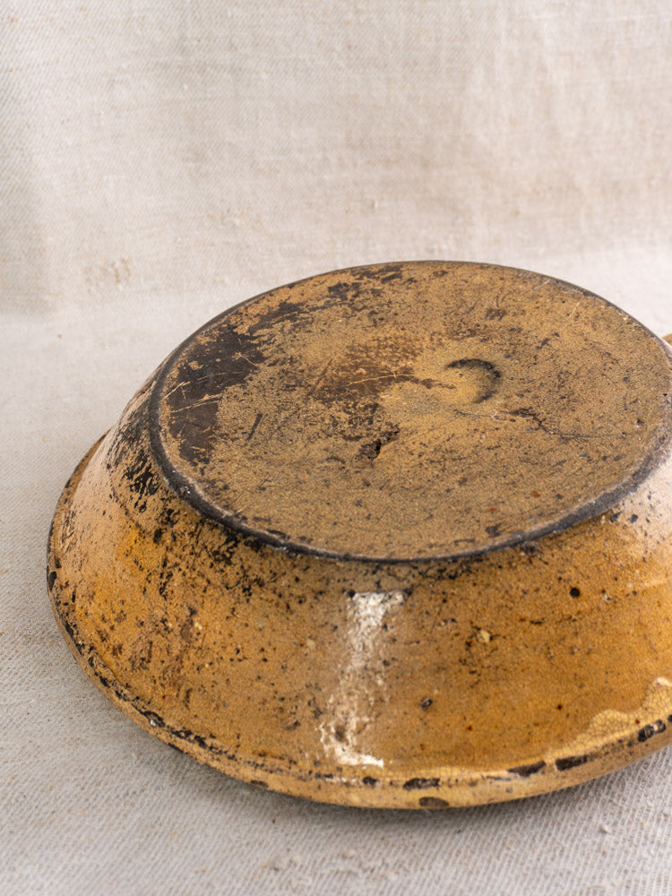 Antique French poêlon from Aubagne, late 18th century, yellow glaze, upside down on beige textured fabric showing unglazed base.