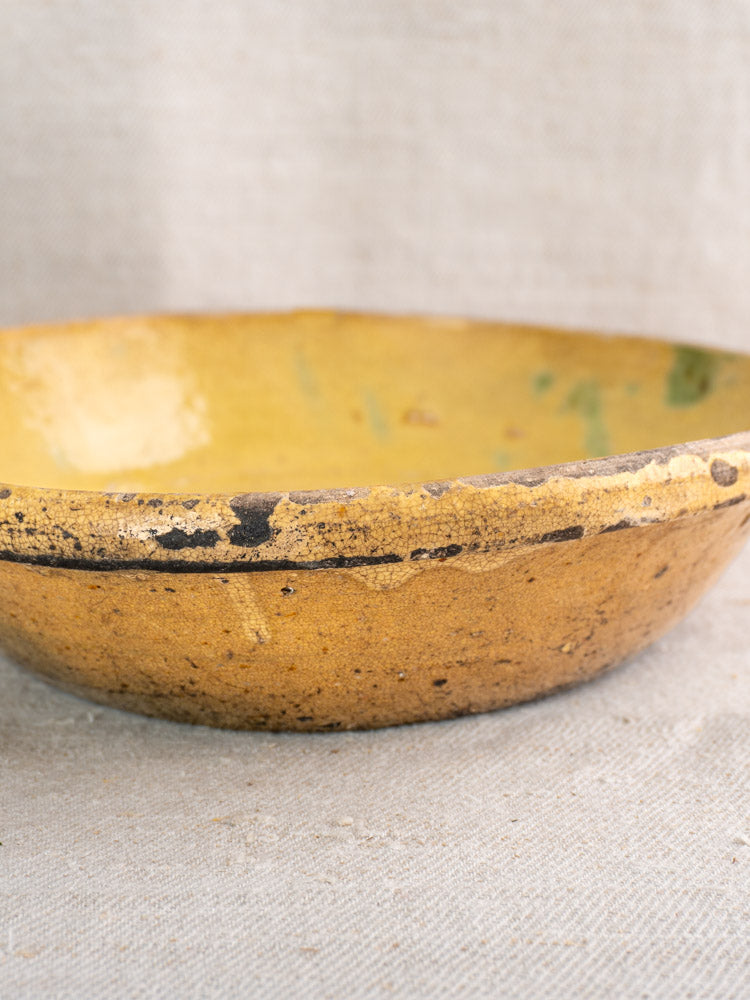 Antique French Poêlon from Aubagne, late 18th-century terracotta bowl with yellow glaze and chipped rim on neutral fabric.