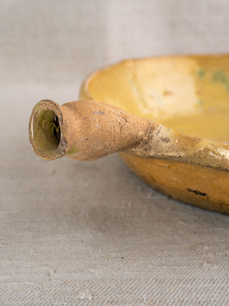 Antique French poêlon in yellow-glazed terracotta with spout handle and rustic finish on beige fabric.
