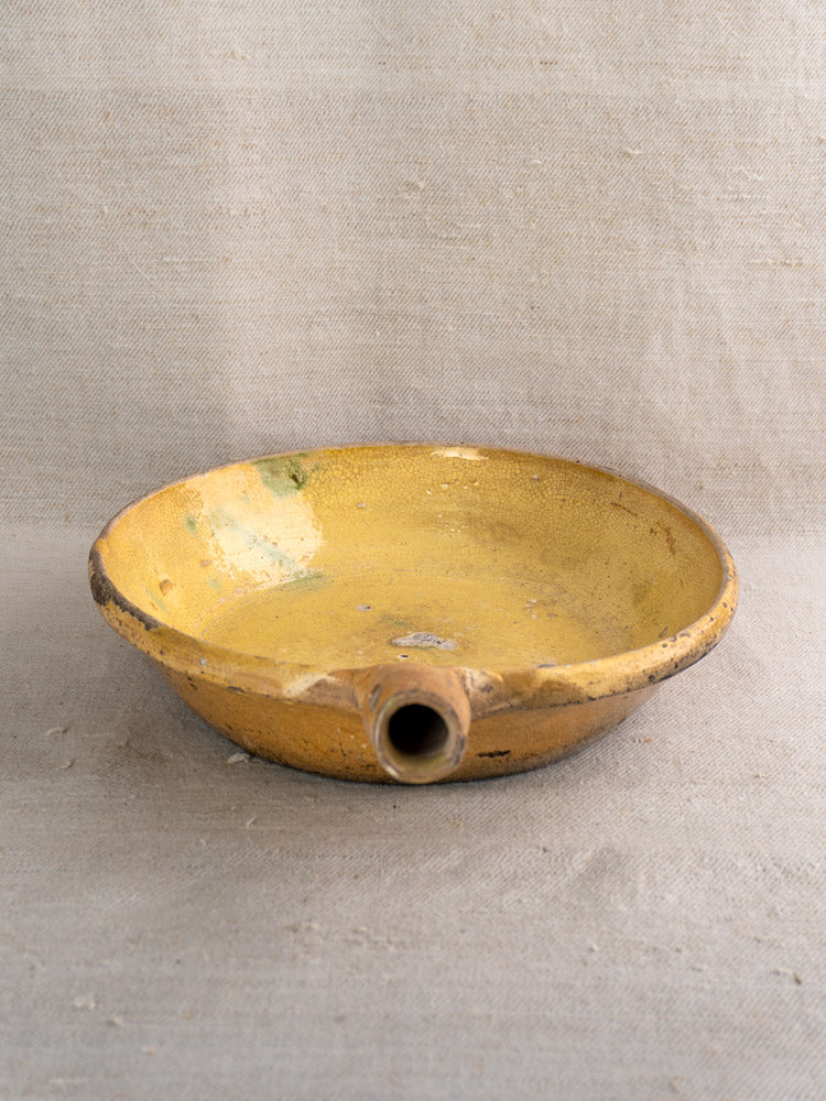 Antique French Poêlon from Aubagne with yellow glaze and spout on beige fabric, showing Provençal terracotta pottery details.