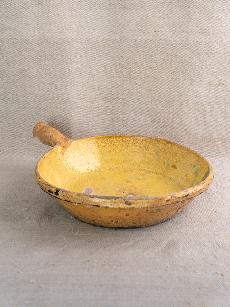 Antique French poêlon, late 18th-century terracotta bowl with yellow glaze and side handle, displayed on burlap.