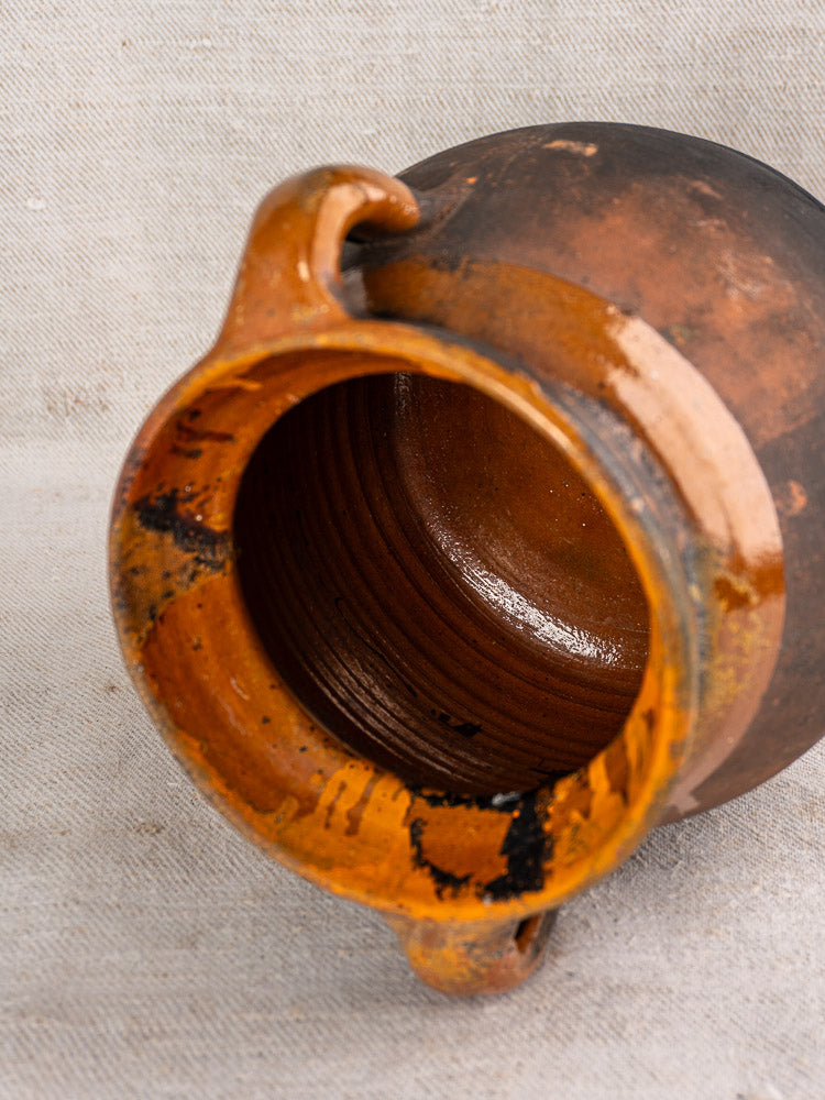 Antique French earthenware confit pot with wide mouth, double handles, and glazed interior on a light fabric surface.
