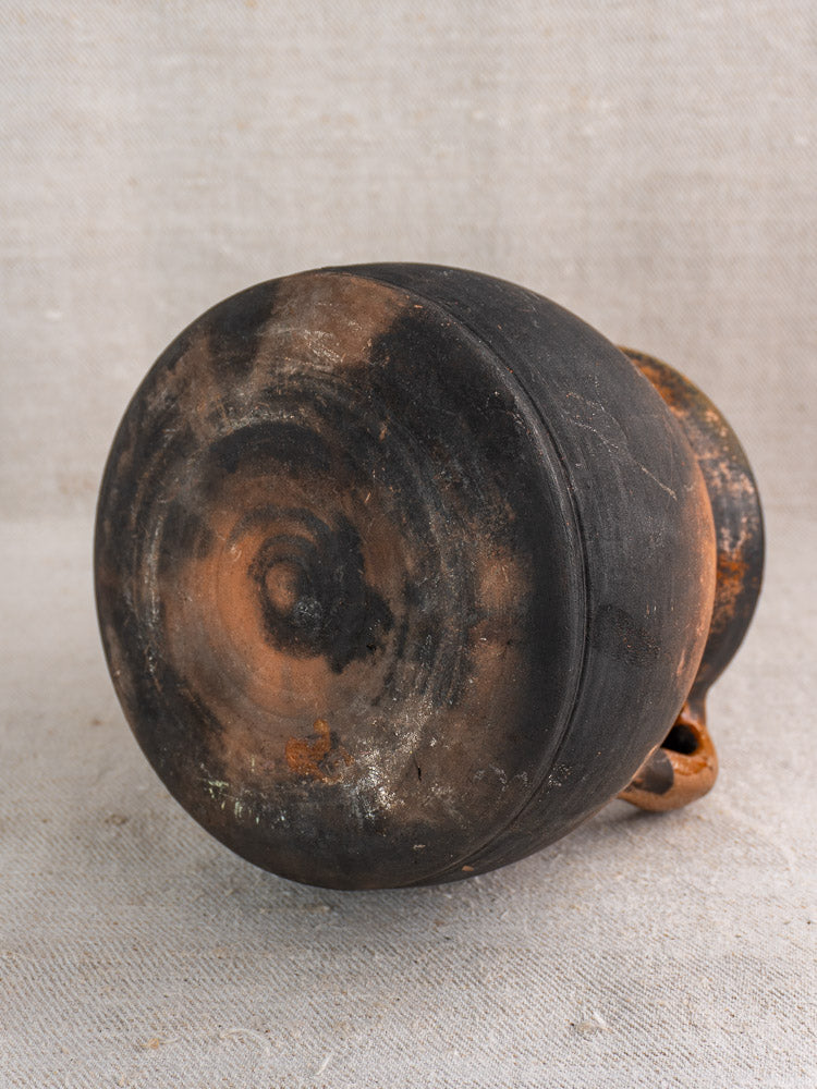 Antique French earthenware confit pot, late 19th century, upside down on beige fabric with blackened finish and loop handle.