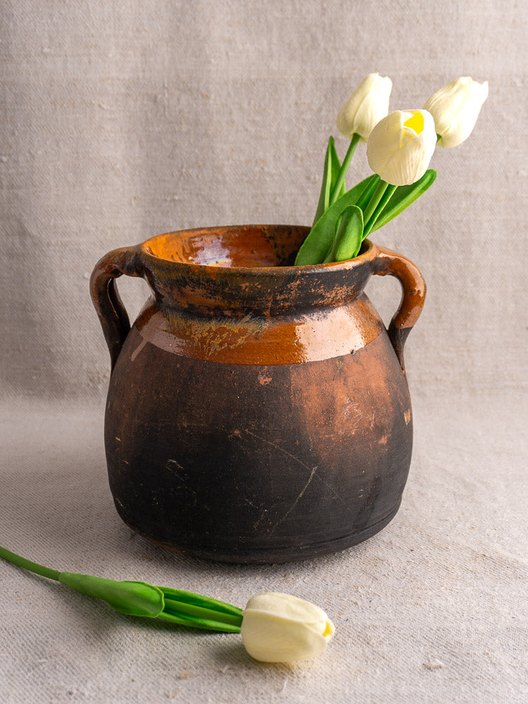Late 19th-century French earthenware confit pot with two handles, holding white tulips on neutral textured fabric.