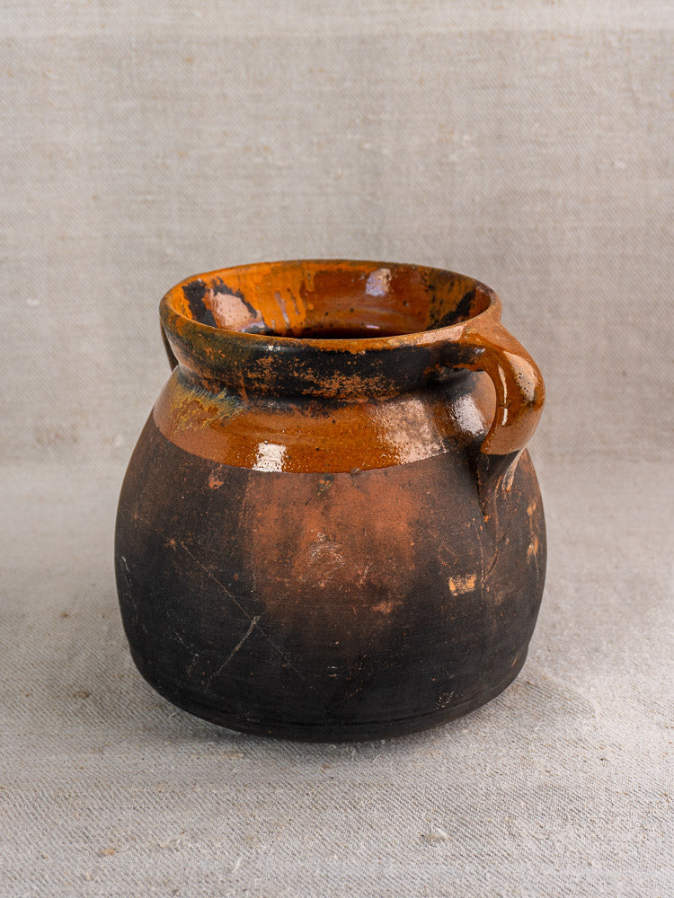 Antique French confit pot, late 19th-century earthenware with round shape, curved handle, and contrasting brown glaze.