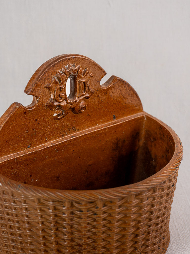 Antique French salt-glazed stoneware salt box with GD initials and keyhole top, on pale fabric surface.