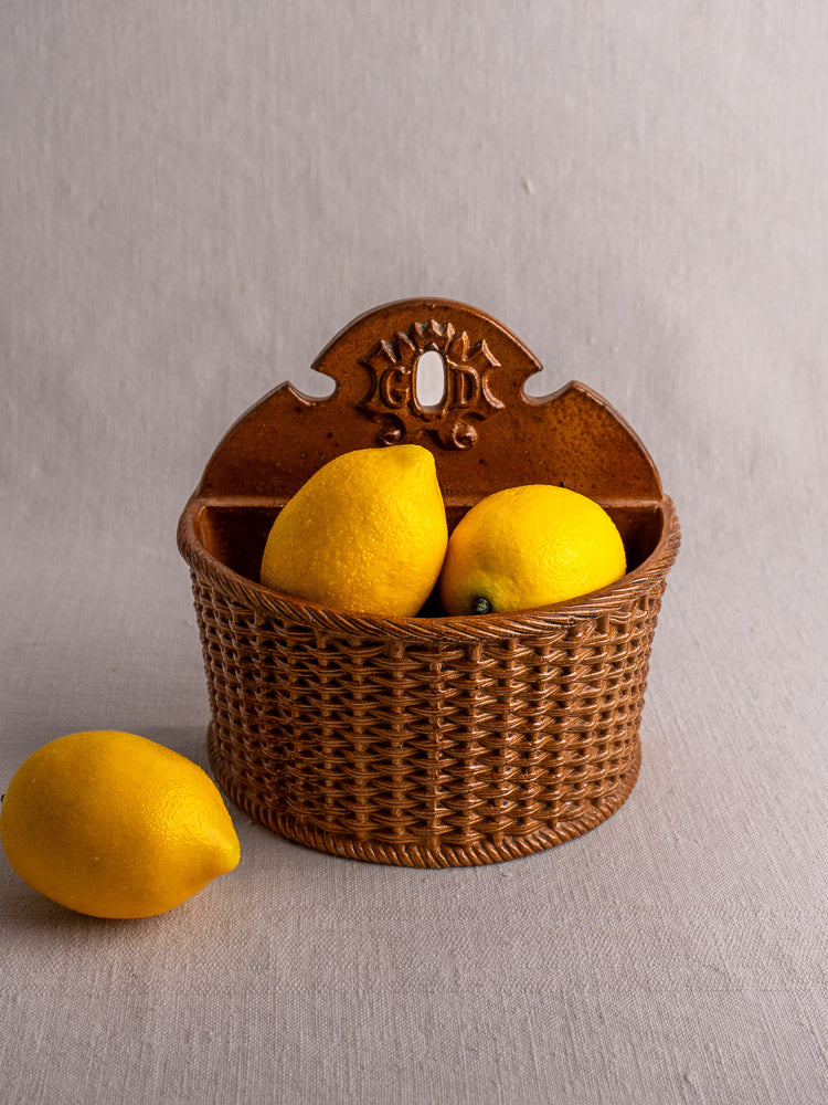 Antique French salt-glazed stoneware salt box with woven pattern, two lemons inside, third lemon on pale gray fabric.