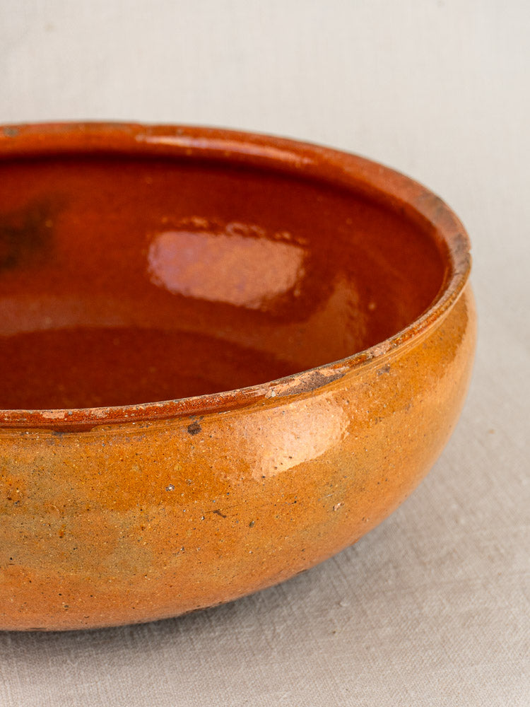 Antique French Vallauris terracotta poêlon with glossy interior, matte exterior, on a light textured background.