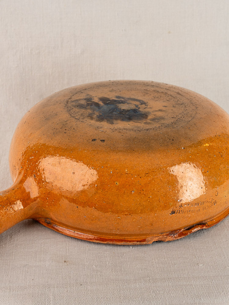Early 20th century Vallauris glazed terracotta poêlon upside down, orange glaze, burn marks, maker’s mark visible.