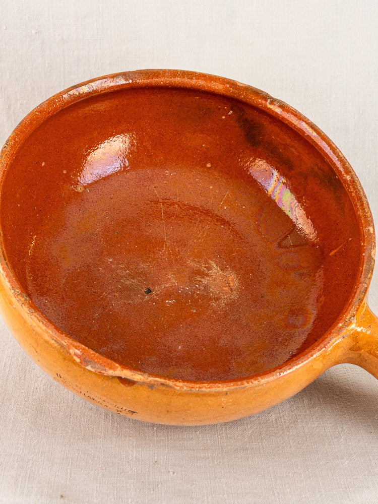 Antique French Vallauris poêlon, early 20th century terracotta with handle, on light neutral fabric.