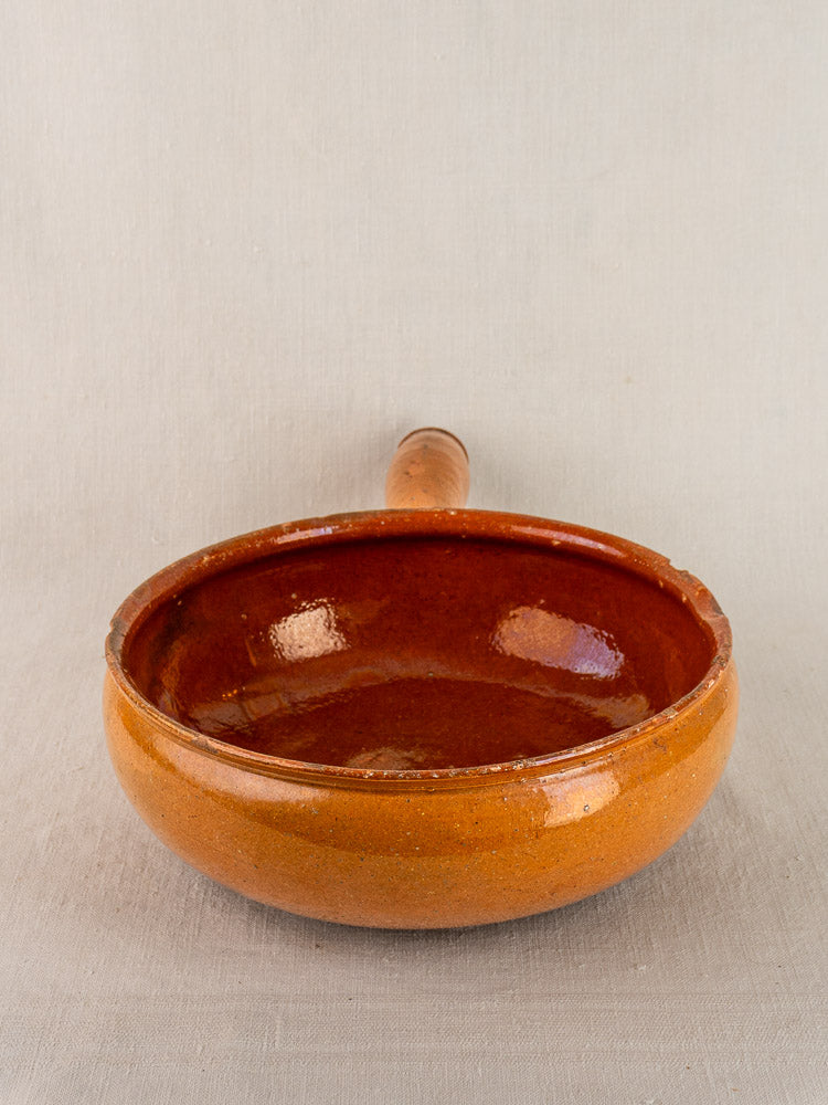 Antique French Vallauris poêlon, early 20th-century glazed terracotta, single handle, on light gray surface.