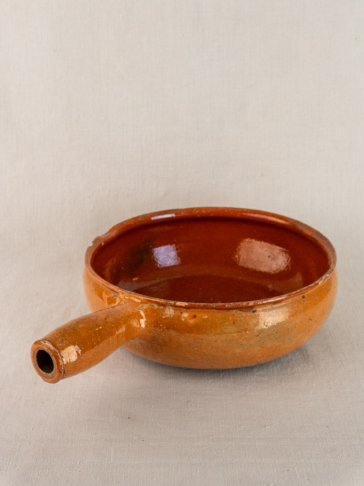 Early 20th-century Vallauris glazed terracotta French poêlon with single spout handle on neutral fabric background.