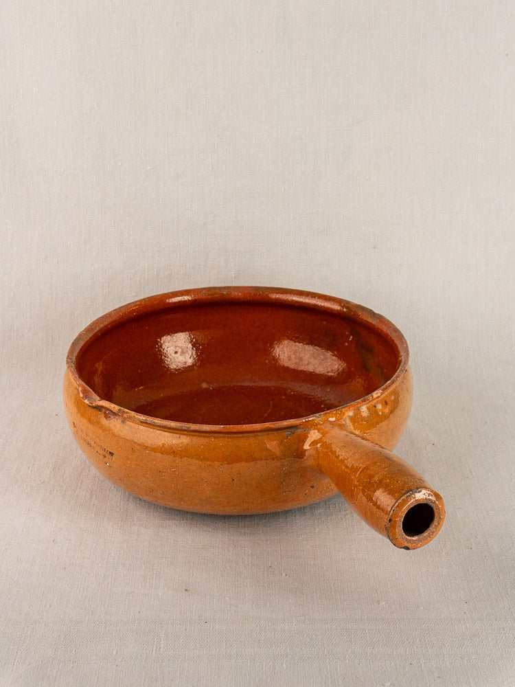 Early 20th-century Vallauris French poêlon in glazed terracotta with single spout, on a light gray background.