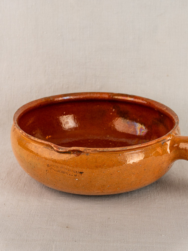 Early 20th-century French Vallauris glazed terracotta poêlon with handle and spout, set on light gray background.