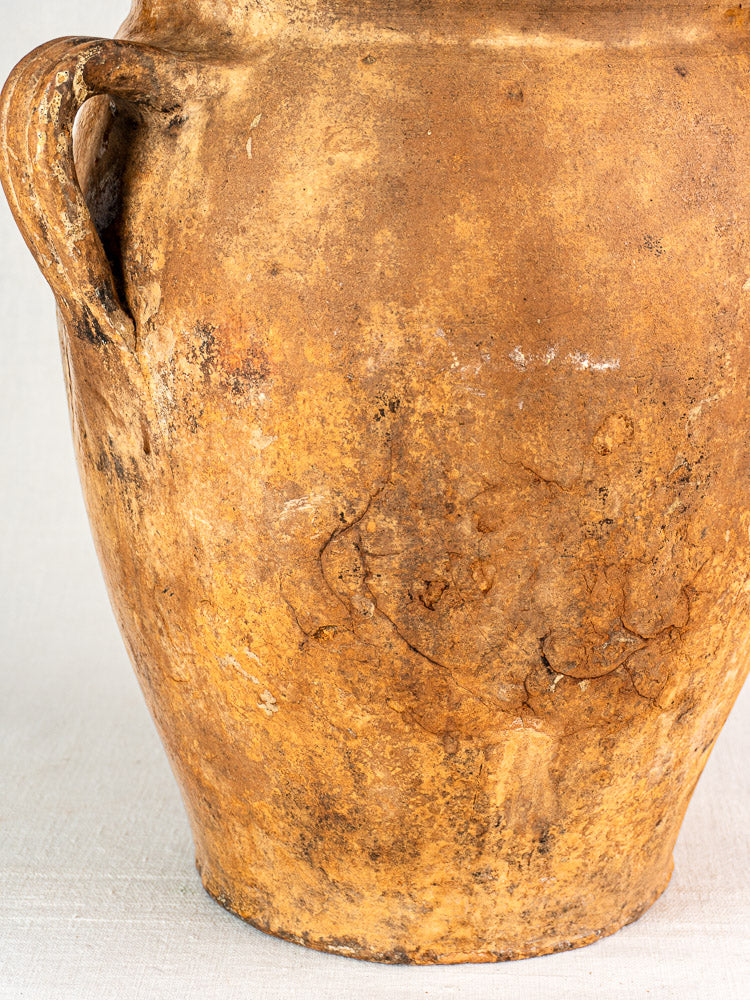 Antique French terracotta storage jar with weathered brown exterior, single handle, and yellow glazed interior.