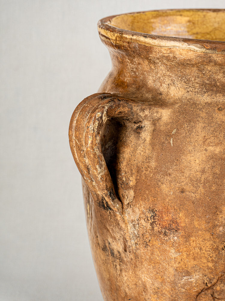 Antique French terracotta storage jar with weathered clay, curved handle, and yellow-glazed rim.