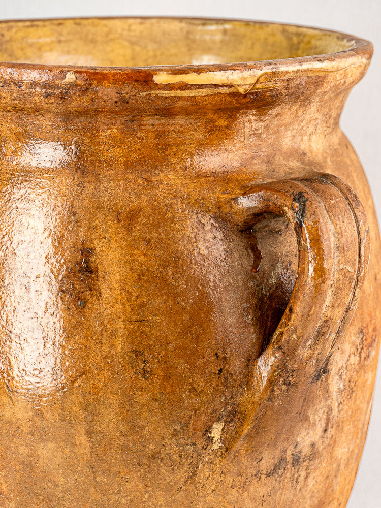 Antique French terracotta storage jar with textured brown ceramic, curved handle, and yellow-glazed interior.