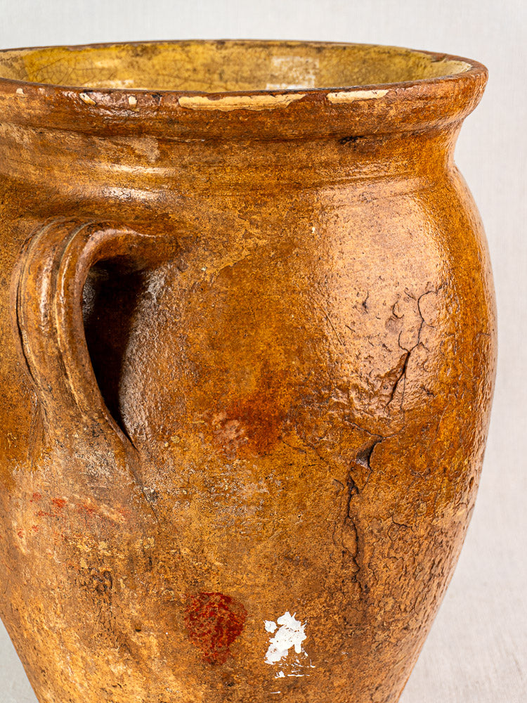 Antique French terracotta storage jar with single handle, textured brown surface, patina, yellow glazed interior.