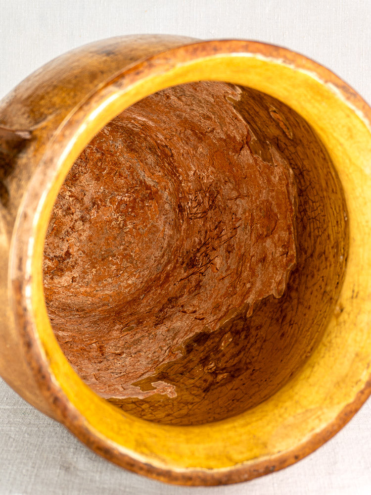 Close-up of antique French terracotta storage jar with yellow-glazed textured interior and glossy rim.