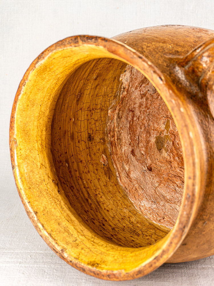 Antique French terracotta storage jar with rustic brown exterior, yellow glazed interior, aged cracks, textured wear.