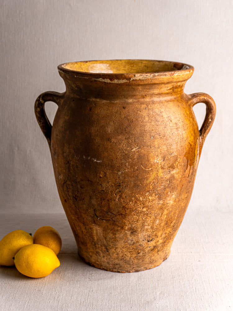 Antique French terracotta storage jar with yellow glazed interior and two handles beside three lemons.