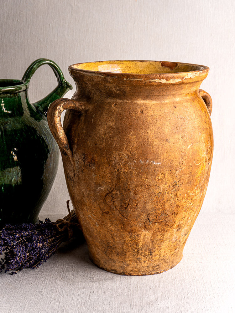 Antique French terracotta storage jar with yellow glaze and twin handles beside a green jug and dried lavender.
