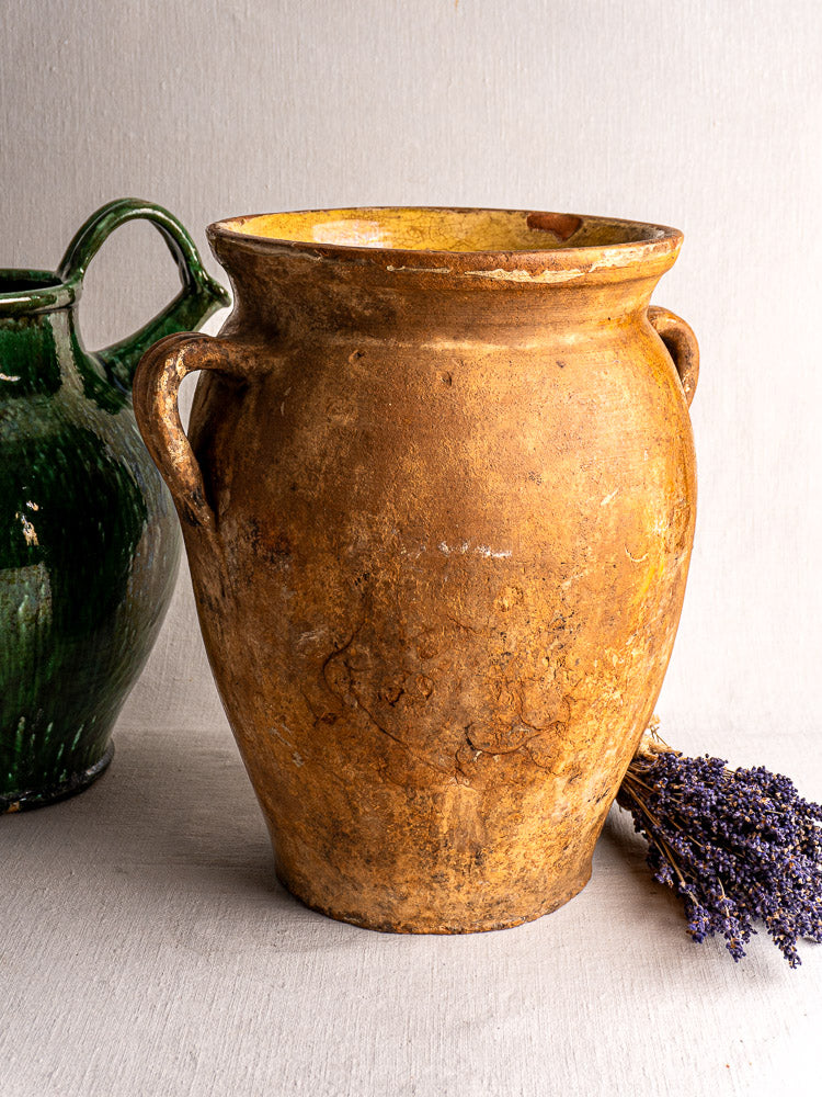 19th-century French terracotta storage jar with yellow glazed interior and side handles, next to a green jug and dried lavender.