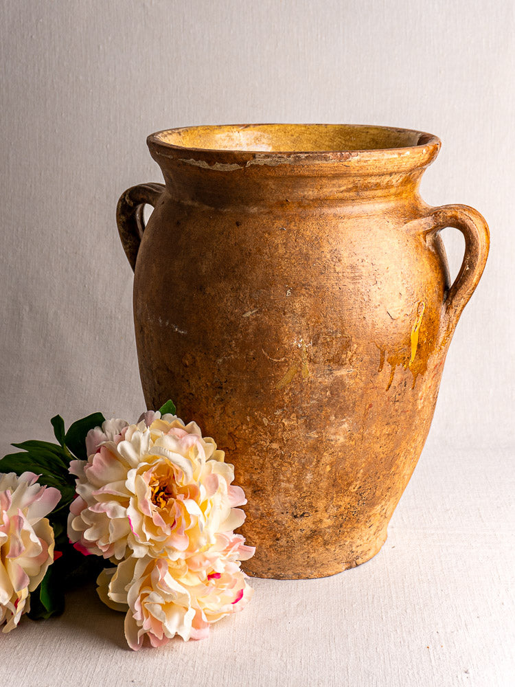 19th-century French terracotta storage jar with yellow glazed interior, two handles, and peonies on a light surface.
