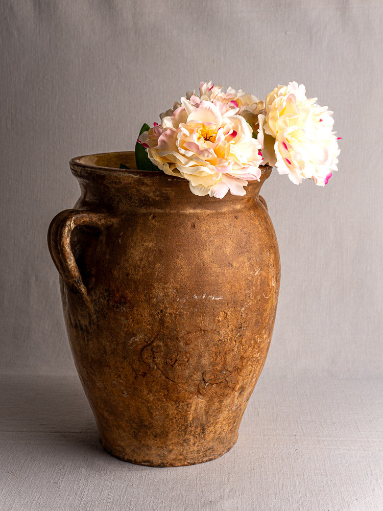 Antique French terracotta storage jar with yellow glazed interior and three pale pink peonies.