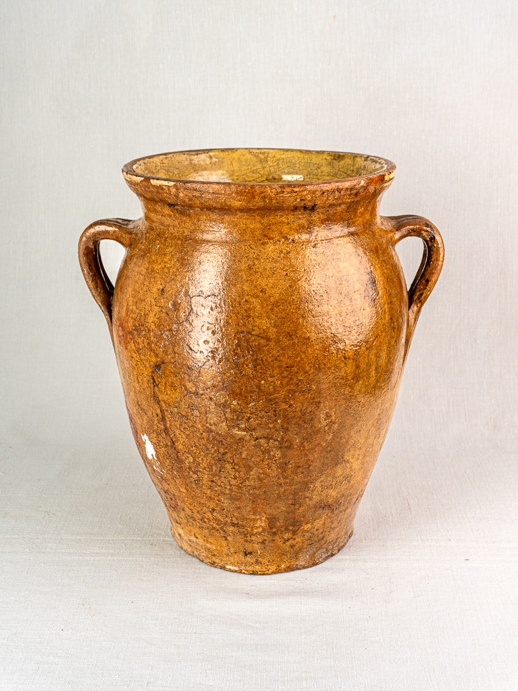 19th-century French terracotta storage jar with two handles and yellow glazed interior on gray surface.