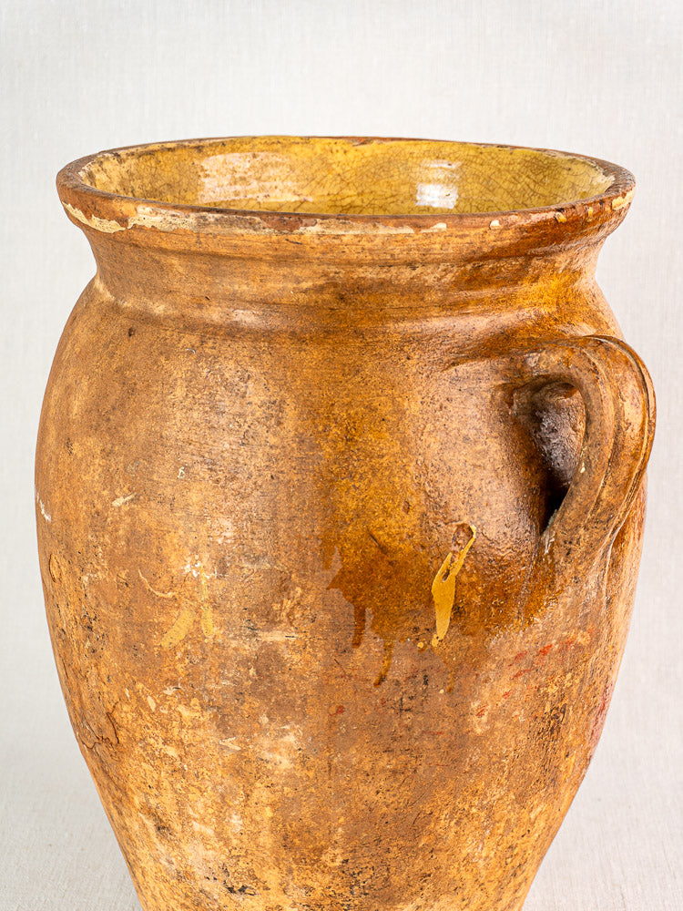 Antique French terracotta storage jar with rustic brown ceramic, single handle, yellow glazed interior.