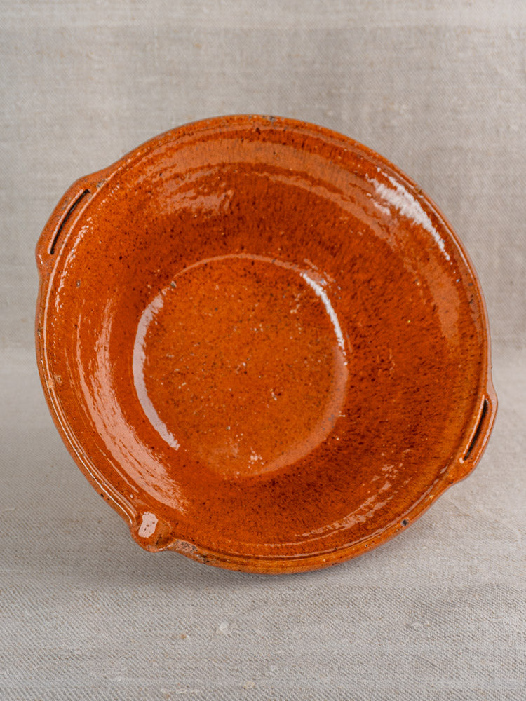Antique French Languedoc tian bowl, glazed earthenware, orange-brown, two handles, on beige fabric.