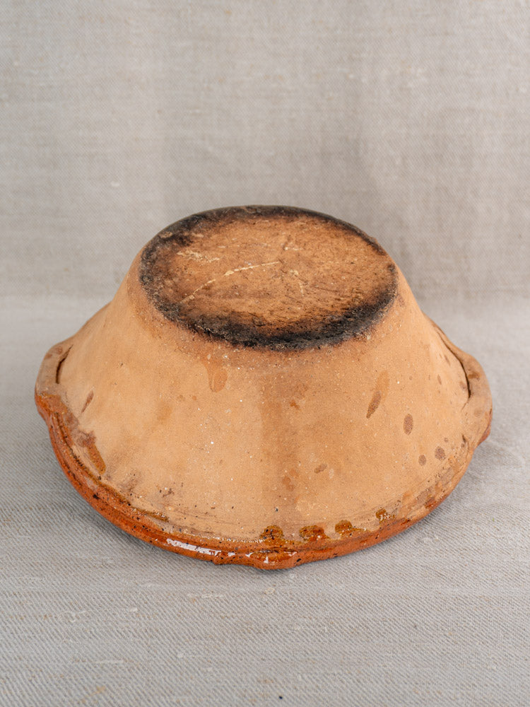 Upside-down rustic brown ceramic tian bowl with weathered base on light gray textured fabric.