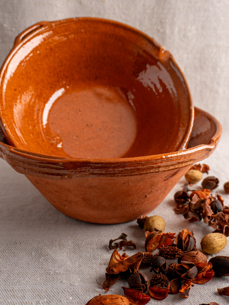 Antique French Languedoc glazed earthenware tian bowls stacked on beige fabric with dried spices nearby.