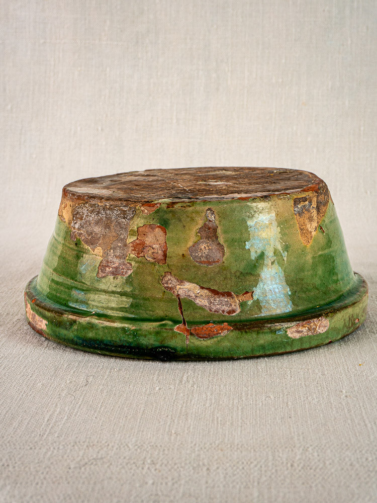 Antique French Tian bowl with green and yellow glaze, terracotta exposed, on beige textured surface.