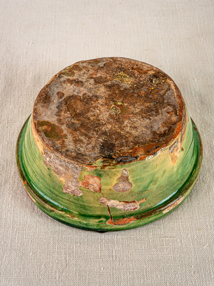 Antique French terracotta Tian bowl with green-yellow glaze, worn base, on light textured fabric.