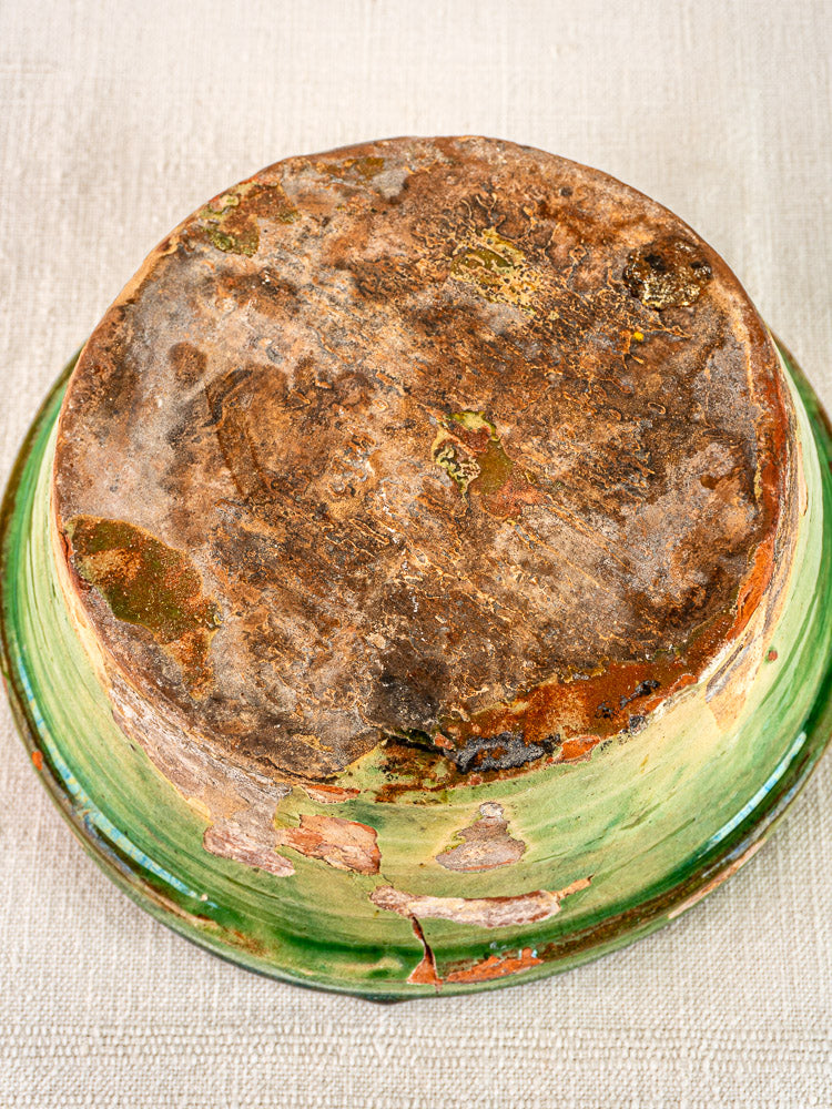 Antique French Tian bowl underside with worn glaze, discoloration, and exposed clay on beige surface.