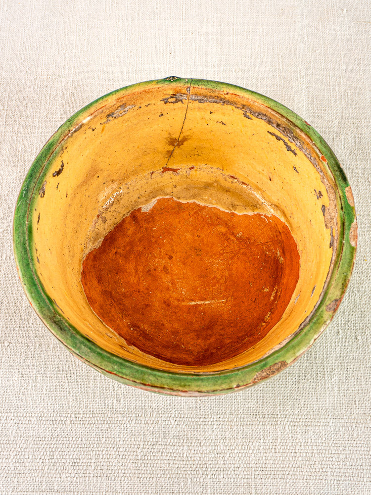 Antique French Tian bowl in Provençal terracotta with yellow glaze, green rim, and aged patina on beige fabric.